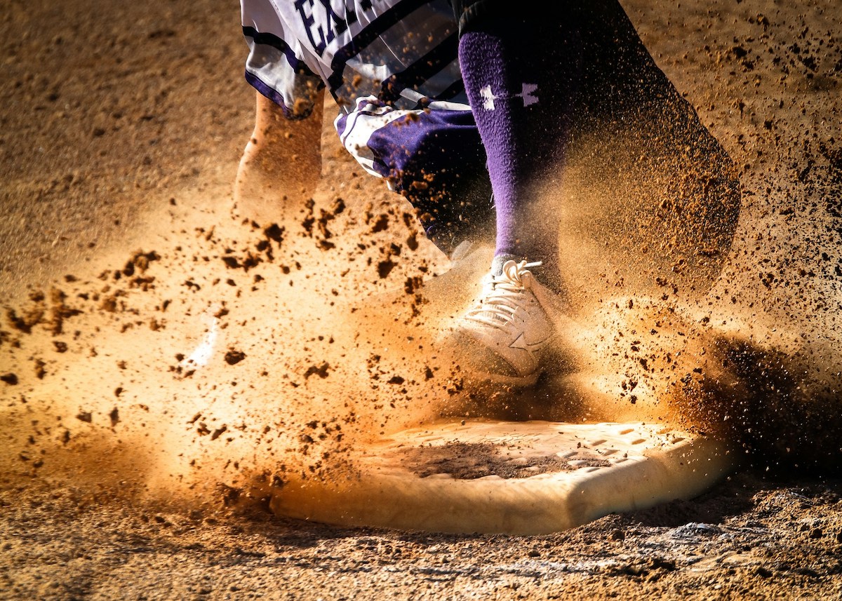 A baseball player sliding into a base while kicking up dirt.