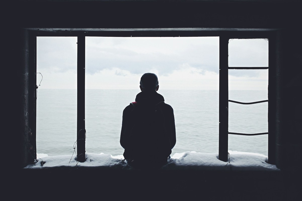 Silhouette of a man looking out a window over a body of water.