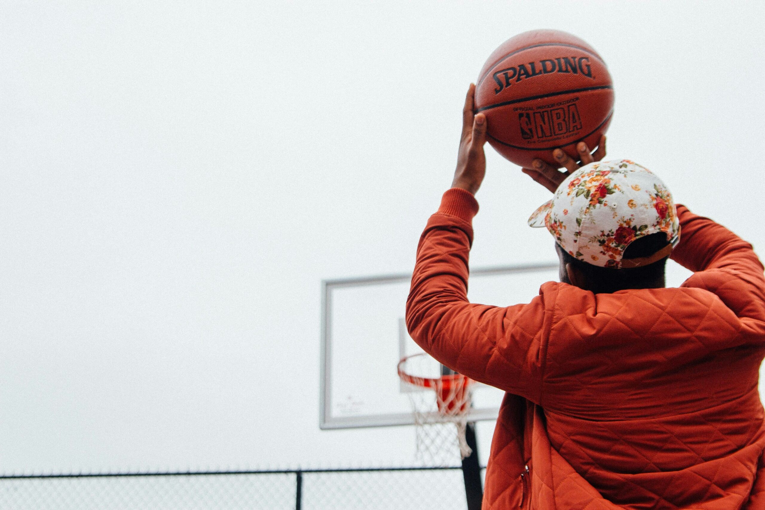 Man in a jacket shooting a basketball at a hoop.